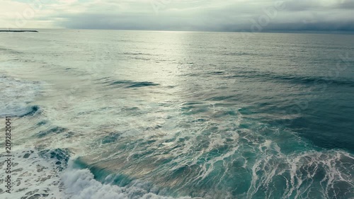Aerial drone view of dark ocean waves reflecting sunlight near Pacific Beach under dramatic cloudy California skies above