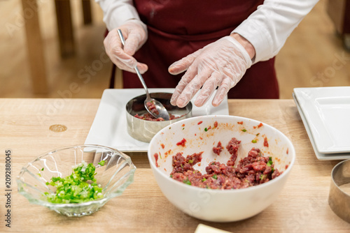 Foto Hands with gloves preparing raw seasoned ground meat in a round mold for food pl