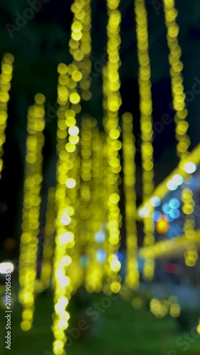 Vertical 4K video. 60 fps. Street city decor with garland is out of focus for New Year 2027. Blurred background with golden bokeh lights. Concept of celebration, fun, joy, winter holiday, carnival