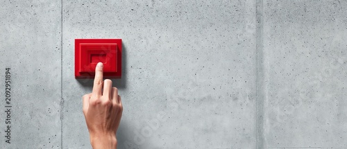 Hand pressing a red emergency alarm button.
