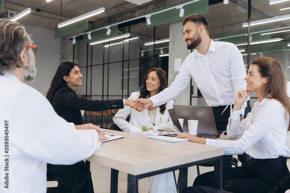 Fototapeta premium Business team members shake hands in a modern office, collaborating to finalize an agreement in a thriving corporate setting