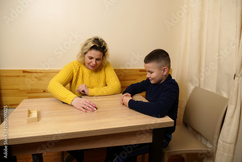 Mother and son play dominoes at the kitchen table, carefully plan their moves, develop logic, and enjoy time together.