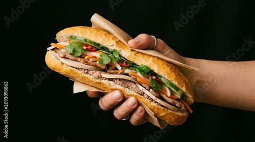 Hand holding a large overstuffed deli sandwich with fresh vegetables and meat.