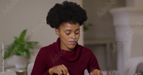 Woman in burgundy sweater cutting food with knife and fork at dining table hearing voice responding