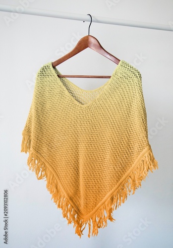 фотографія Yellow knitted poncho with fringe detail hanging on a wooden hanger