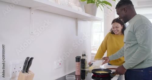 African American couple pouring eggs into pan, adding chopped tomatoes, preparing meal at kitchen