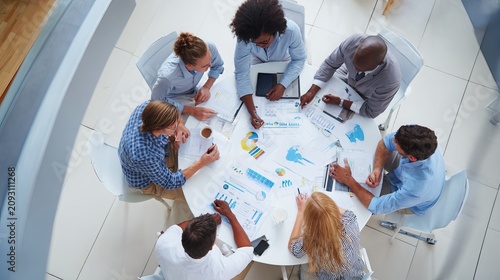 High angle view of a diverse business team collaborating around a white table reviewing reports charts and strategic planning documents during a productive meeting in a bright modern open office works