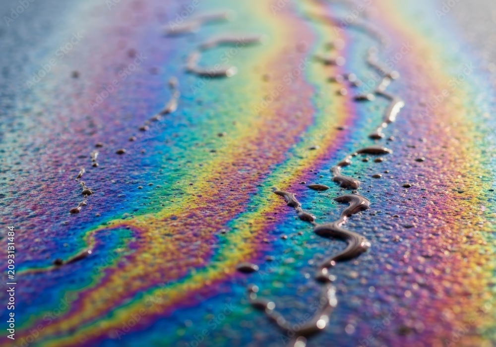 Obraz premium Colorful rainbow oil spill sheen swirling on wet asphalt showing iridescent pollution on a road surface