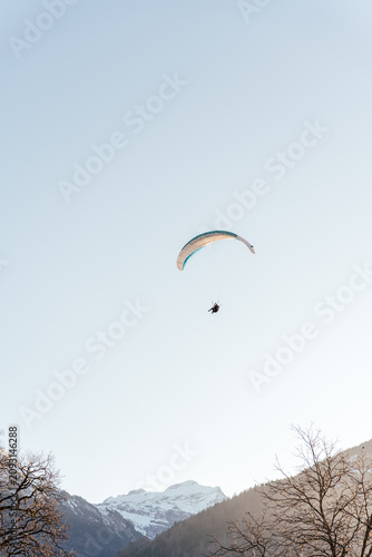 Colorful paraglider soaring above snow capped mountains under a clear blue sky. Scenic alpine landscape creates a powerful adventure and freedom concept perfect for travel and extreme sport themes.