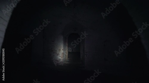 Camera moves through a dark abandoned brick corridor toward an arched doorway, with flashlight illumination revealing a decayed interior and eerie empty passage