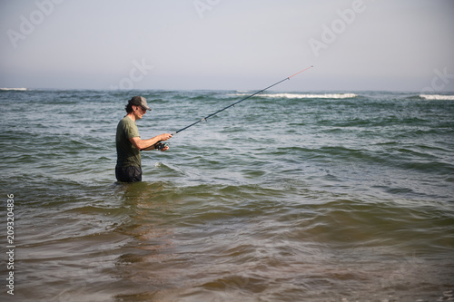 Man fishing in the sea waist-deep casting a rod on a calm coastal day
