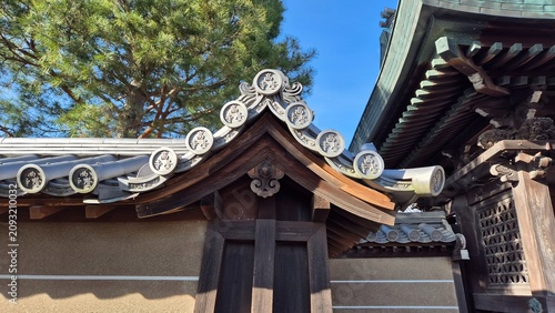 Close-up of traditional Japanese temple roof tiles with kanji characters against a clear blue sky on a sunny day.