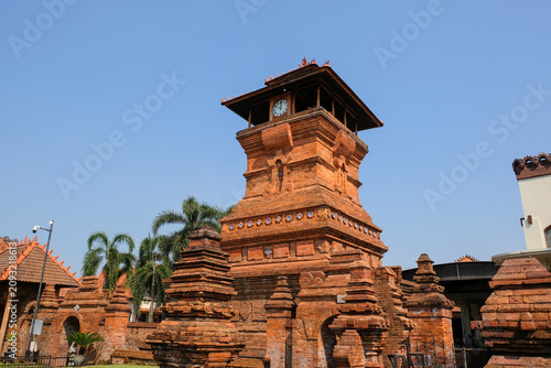 The iconic Menara Kudus mosque tower made of red bricks under a clear blue sky, a historic heritage site blending hindu and islamic architecture in Kudus, Central Java, Indonesia.