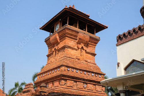 The iconic Menara Kudus mosque tower made of red bricks under a clear blue sky, a historic heritage site blending hindu and islamic architecture in Kudus, Central Java, Indonesia.