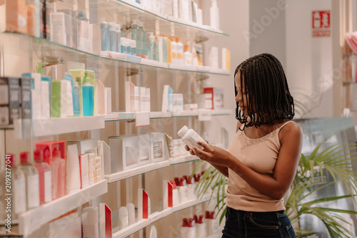 Young Hispanic woman reading product label while standing in pharmacy