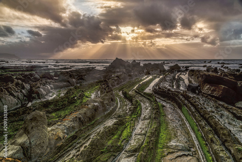 Photography Powerful sunbeams breaking through dark storm clouds over mossy flysch rock form
