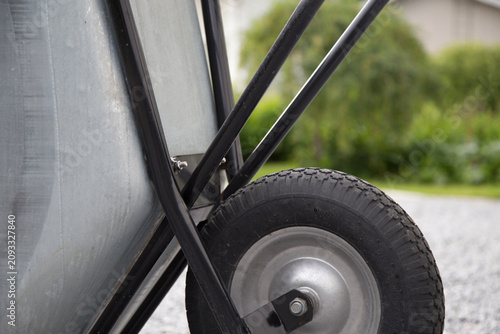 Close-up picture of galvanized garden cart for transporting soil, gravel and plants in the backyard. Heavy-duty garden utility wheelbarrow with pneumatic wheel for yard and landscaping work.