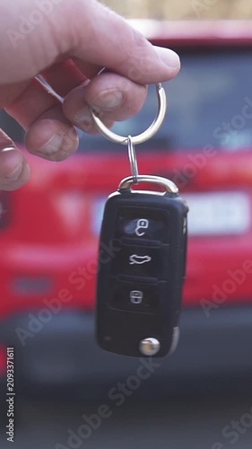 Close-up of a person holding a black car remote key fob, preparing to unlock a vehicle.
