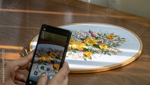 Artisan Taking Photo of Finished Floral Embroidery Hoop with Smartphone for Social Media