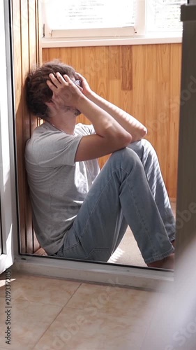 Depressed man sitting on balcony floor holding head in hands suffering from panic attack