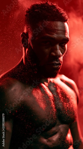 Intense portrait of a muscular Black man with sweat and red lighting
