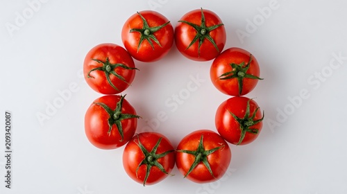 A top-down composition of tomatoes arranged in a circular pattern on a clean white surface with green stems for contrast