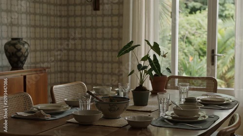 Inviting Dining Room Interior with Set Table and Green Potted Plants, Bathed in Natural Light from