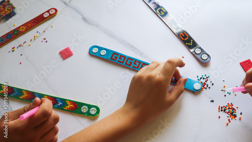sister and brother are making crafts from diamond mosaics in the form of bracelets on a table in the room close-up