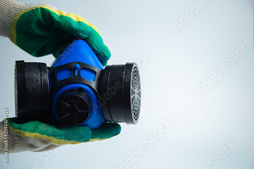 Hands in construction gloves holding a protective blue mask with two filters on a white background with space for text. Concept of personal protective equipment, respiratory protection, repair. High