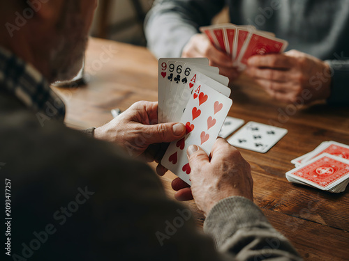 Hands holding playing cards at a wooden table for leisure and entertainment, close up view