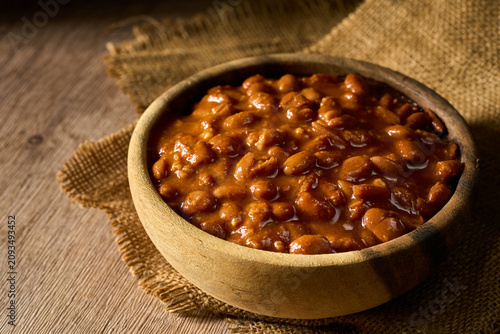 closeup homemade classic cowboy meal or pinto bean in a wooden bowl on a table. Savory stewed baked bean with rich sauce, background with copy space