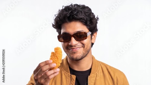 Young man wearing sunglasses eating crispy snack, smiling while enjoying crunchy food on white background