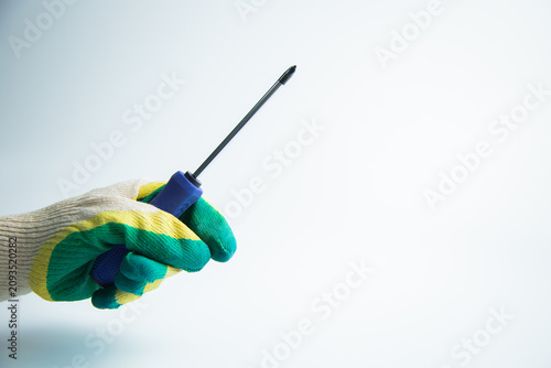 Close-up of a gloved hand holding a screwdriver on a white background. The concept of repair, twisting, handyman, construction, tools. High quality photo