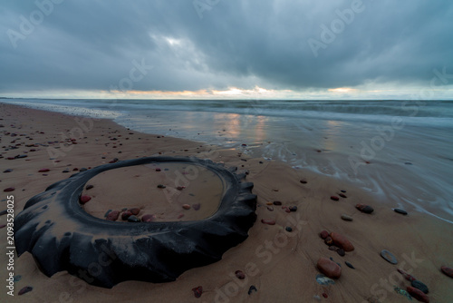 Old tire on sandy beach under dark cloudy sky