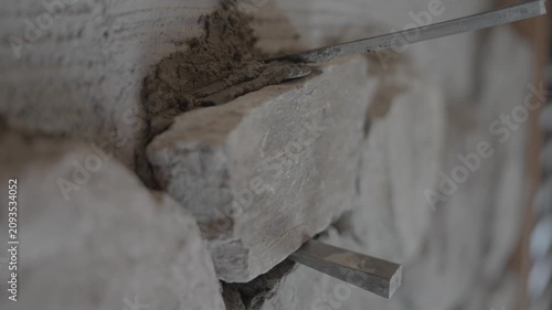 Close-up video of a craftsman using a small trowel to carefully spread and smooth wet mortar around the edges of a newly placed stone on a wall. 