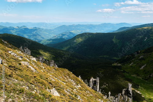 Cuadro en lienzo A horizontal high-angle shot of tall stone rock formations and rocky pillars on a steep grassy mountainside overlooking a deep green valley, ideal for geology and adventure travel marketing