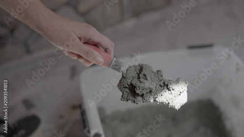 Close-up video of a woman's arms using a hand trowel to scoop wet mortar paste out of a large plastic mixing tub. The footage highlights female representation in skilled trades.