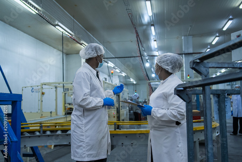 Two engineers in white lab coats discussing operations in a modern industrial facility with machinery