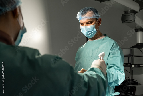 Bild auf Leinwand Man surgeon receives sterile gauze from colleague inside operating room