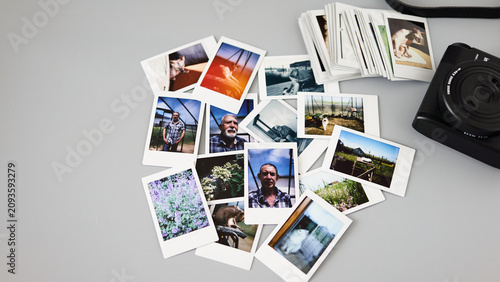 Collection of printed photos scattered on a table beside a camera with images of people and nature