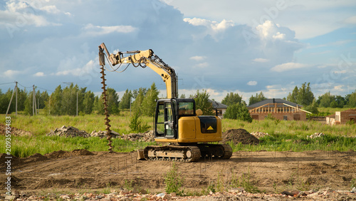 Construction equipment drills into the ground at a building site in a rural area under a cloudy sky during the day