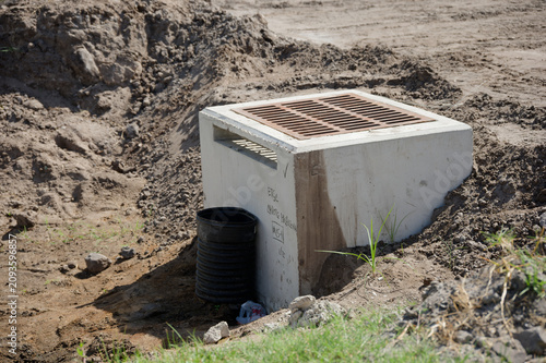 Storm drainage culvert with a metal grate sits partially buried at a construction site, surrounded by excavated soil and sparse grass, illustrating infrastructure, erosion control, and stormwater mana