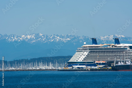 Large cruise ship docked at a port terminal with the snow-covered Olympic Mountain range rising majestically in the background.