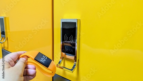 Cuadro en lienzo hand bringing an orange RFID wristband to a contactless electronic lock on a bright yellow locker in a changing room