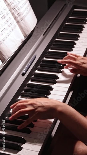 Close-up of piano keys in dark tones as woman plays gentle classical music on digital piano, student practicing piano lessons, vertical video