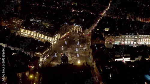 Aerial view of Dam Square in Amsterdam at night, with the Christmas tree, illuminated trees, National Monument, Nieuwe Kerk dome, lit department stores and trams during the holiday season.