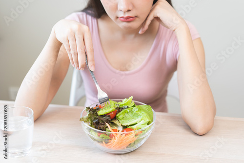 Fotografie Diet in bored face, unhappy beautiful asian young woman, girl on dieting, holding fork at tomato on salad plate, dislike or tired with eat fresh vegetables