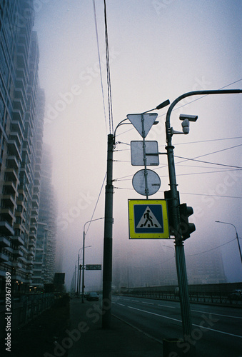Traffic signs and power lines frame a foggy urban highway at dusk