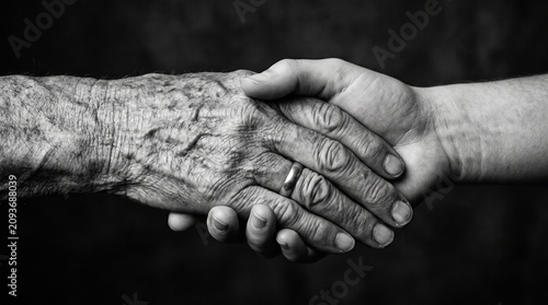 Close-up of elderly person and younger person holding hands in black and white with generations connection wrinkled