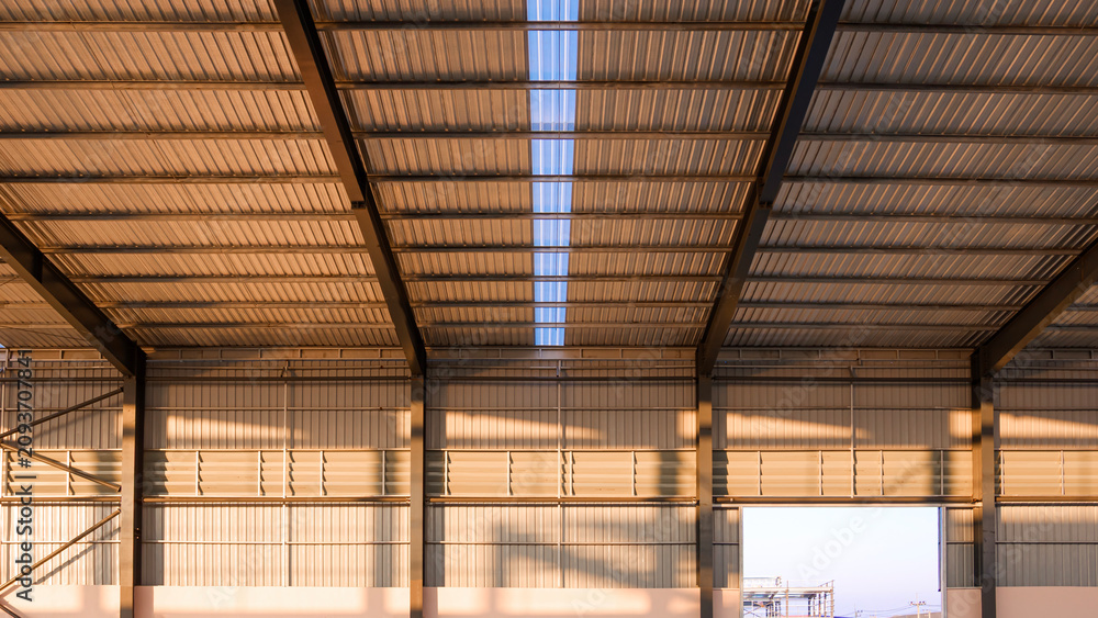 Fototapeta premium Modern empty warehouse interior with metal sheet roof and steel structure under golden evening sunlight in construction site